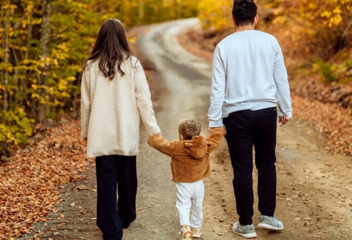 Padres caminando de la mano con su hijo pequeño por un camino al aire libre, simbolizando la formación del carácter y los valores en la vida familiar cotidiana.