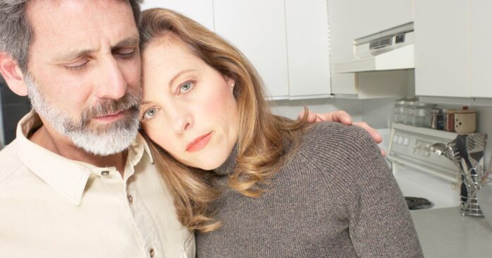 Pareja abrazada en una cocina, con expresión seria y cercana, transmitiendo apoyo mutuo en un momento difícil de la vida en pareja.