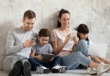 Tecnología y familia: cambios que ya están dentro de casa Familia sentada en el piso de casa usando celulares, tablet y laptop, cada uno concentrado en su propio dispositivo.