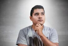 Nadie tiene la vida resuelta a los 20 (aunque en redes parezca que sí) Joven con gesto reflexivo mira hacia arriba mientras sostiene su barbilla con la mano, representando la incertidumbre y la búsqueda de rumbo que muchos experimentan al comenzar la vida adulta.